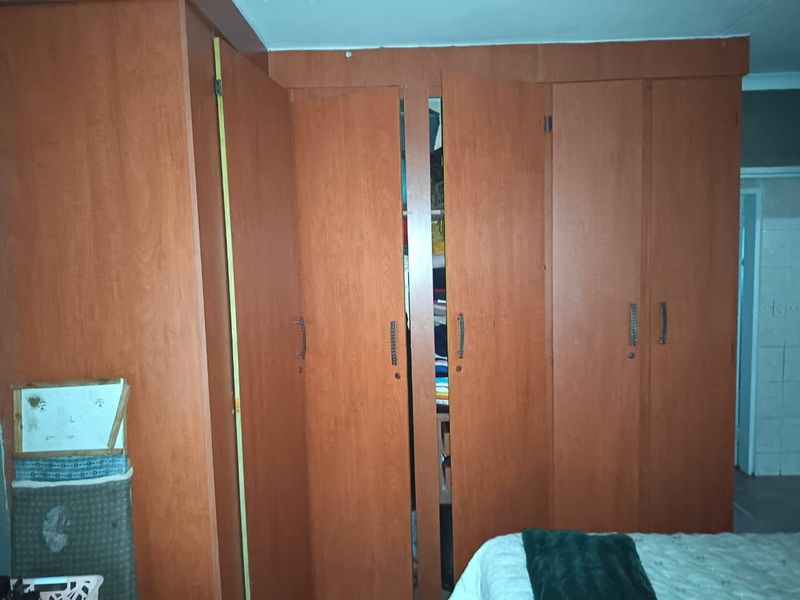 A bedroom featuring dated, built-in wooden cupboards with visible alignment issues and wear, offering potential for modernization.