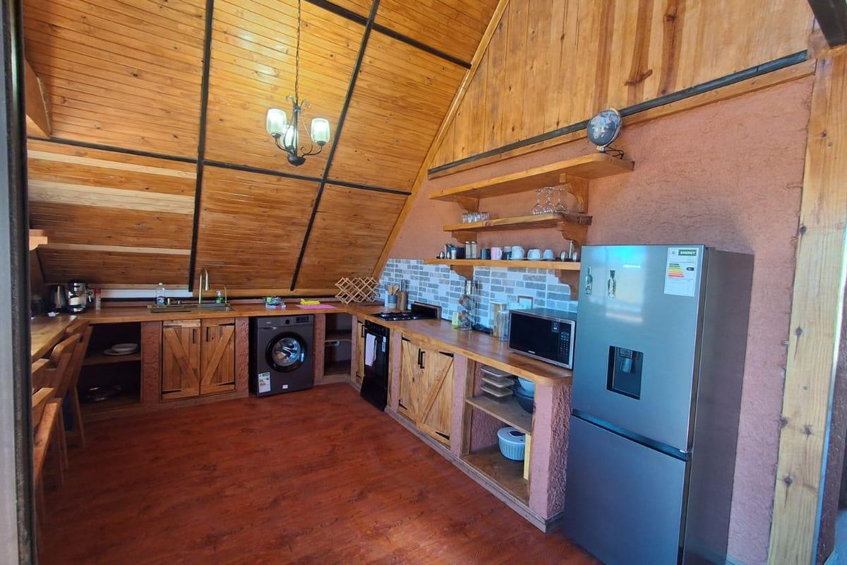 Rustic kitchen featuring vaulted timber ceilings, wooden cabinetry, open shelving, and a tiled backsplash, creating a warm and functional cooking space.