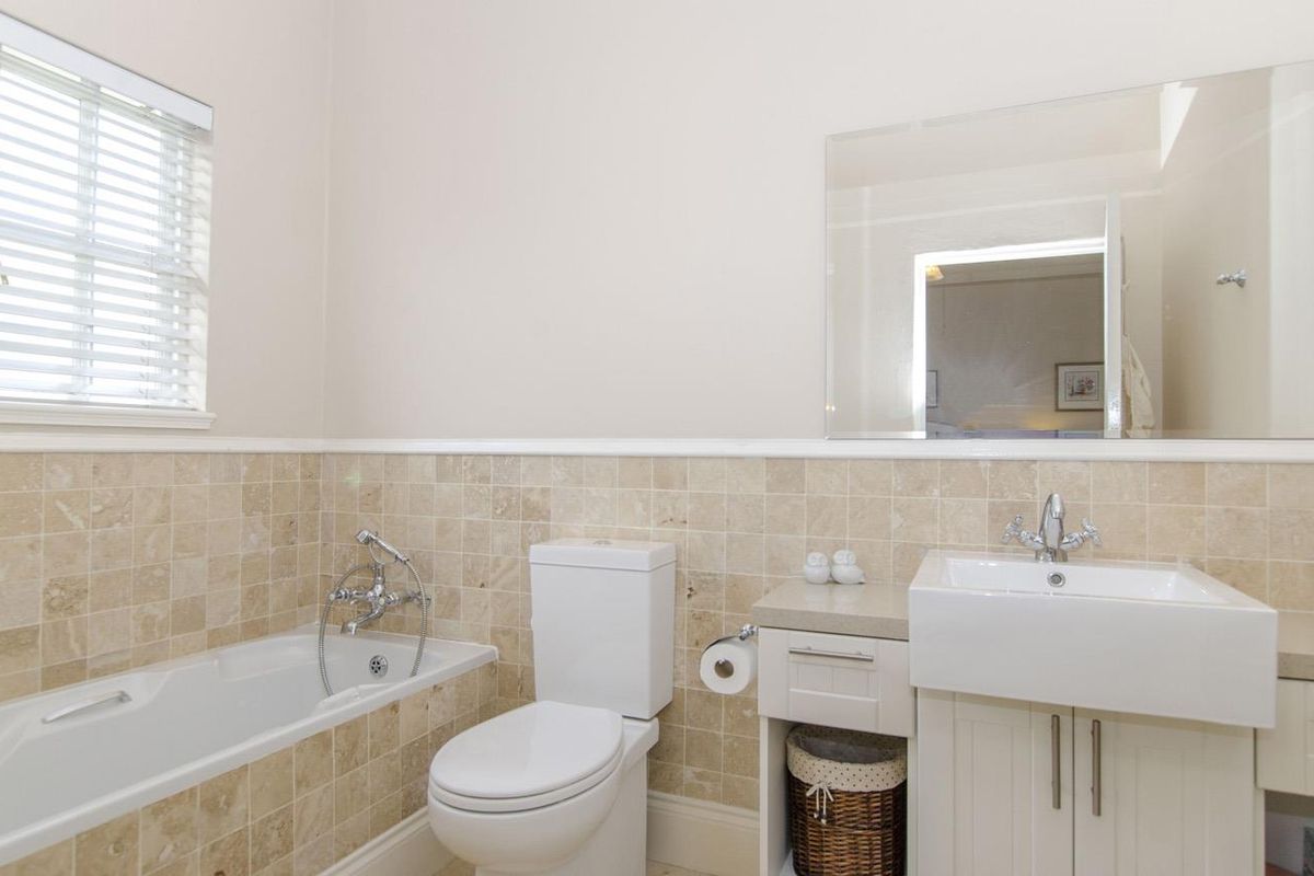 A well-maintained bathroom featuring a built-in bathtub, a modern vanity with a basin, a toilet, and neutral stone-tiled wall accents.