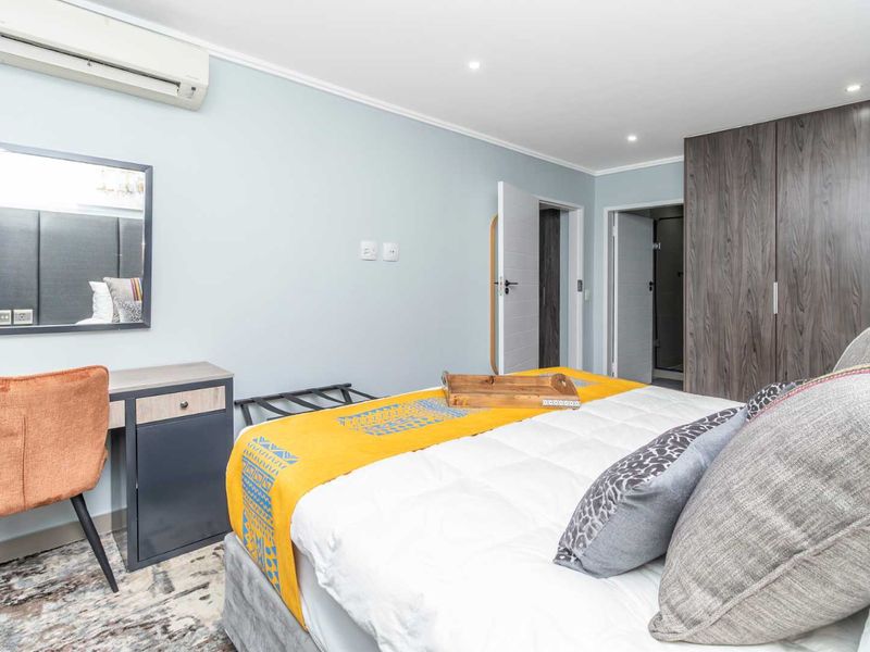 A well-maintained bedroom featuring built-in cupboards, recessed downlighting, and a wall-mounted split-system air conditioner.