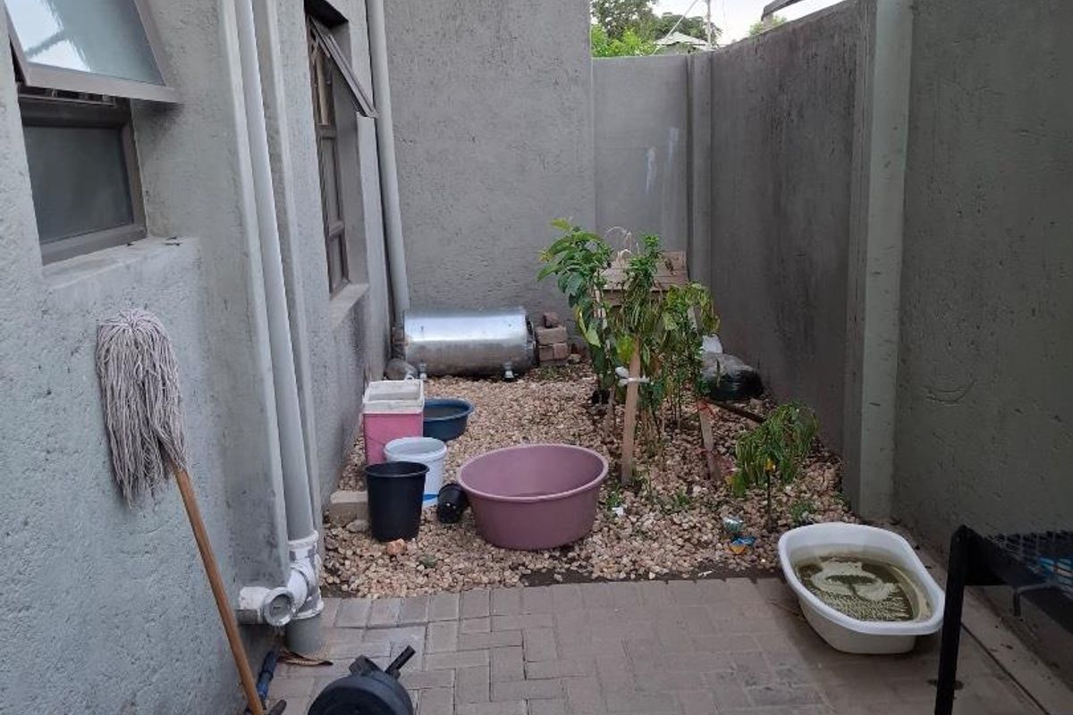 A compact rear courtyard area featuring paved and gravel sections, enclosed by high boundary walls with an external geyser and satellite dish installation.