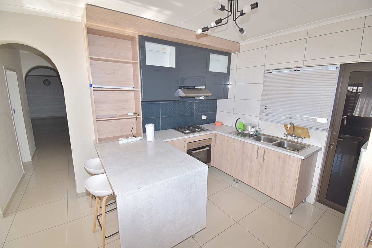 Modern kitchen featuring light wood-tone cabinetry, contrasting grey upper cabinets, built-in oven, gas hob, extractor fan, and a functional breakfast bar island.