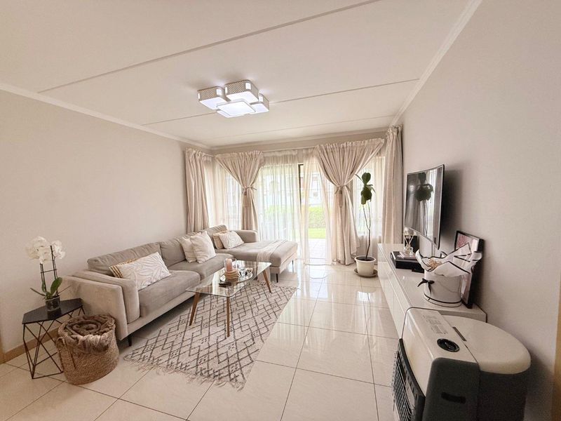 A bright and well-maintained living room featuring neutral tiled flooring and a large sliding glass door providing access to the exterior.