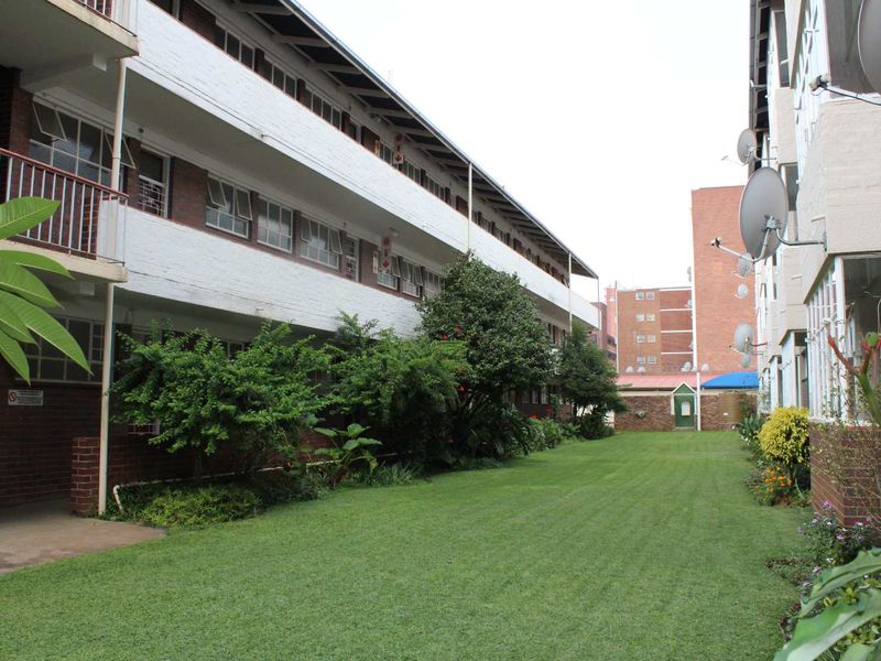 A view of the apartment complex exterior featuring a well-maintained lawn, landscaped garden area, and multi-level balconies with brick facade detailing.