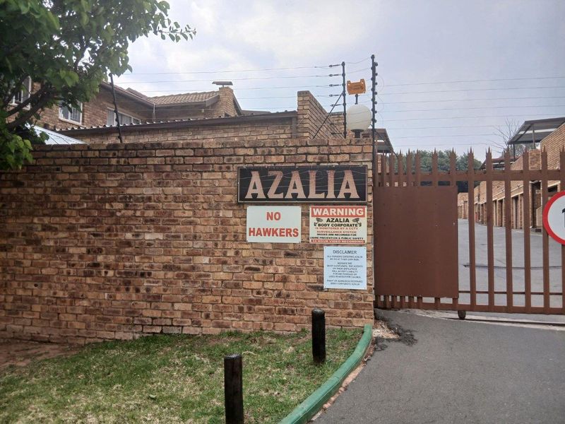 Front entrance view of the Azalia complex featuring a brick boundary wall, secure metal gate, and integrated CCTV security infrastructure.