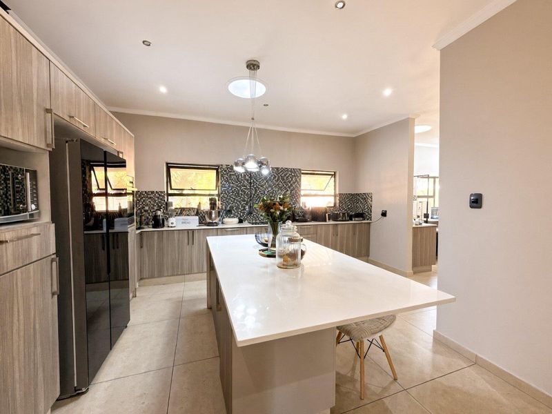 Modern kitchen featuring a large central island with quartz countertops, extensive built-in cabinetry, mosaic tile backsplash, and contemporary recessed and pendant lighting.