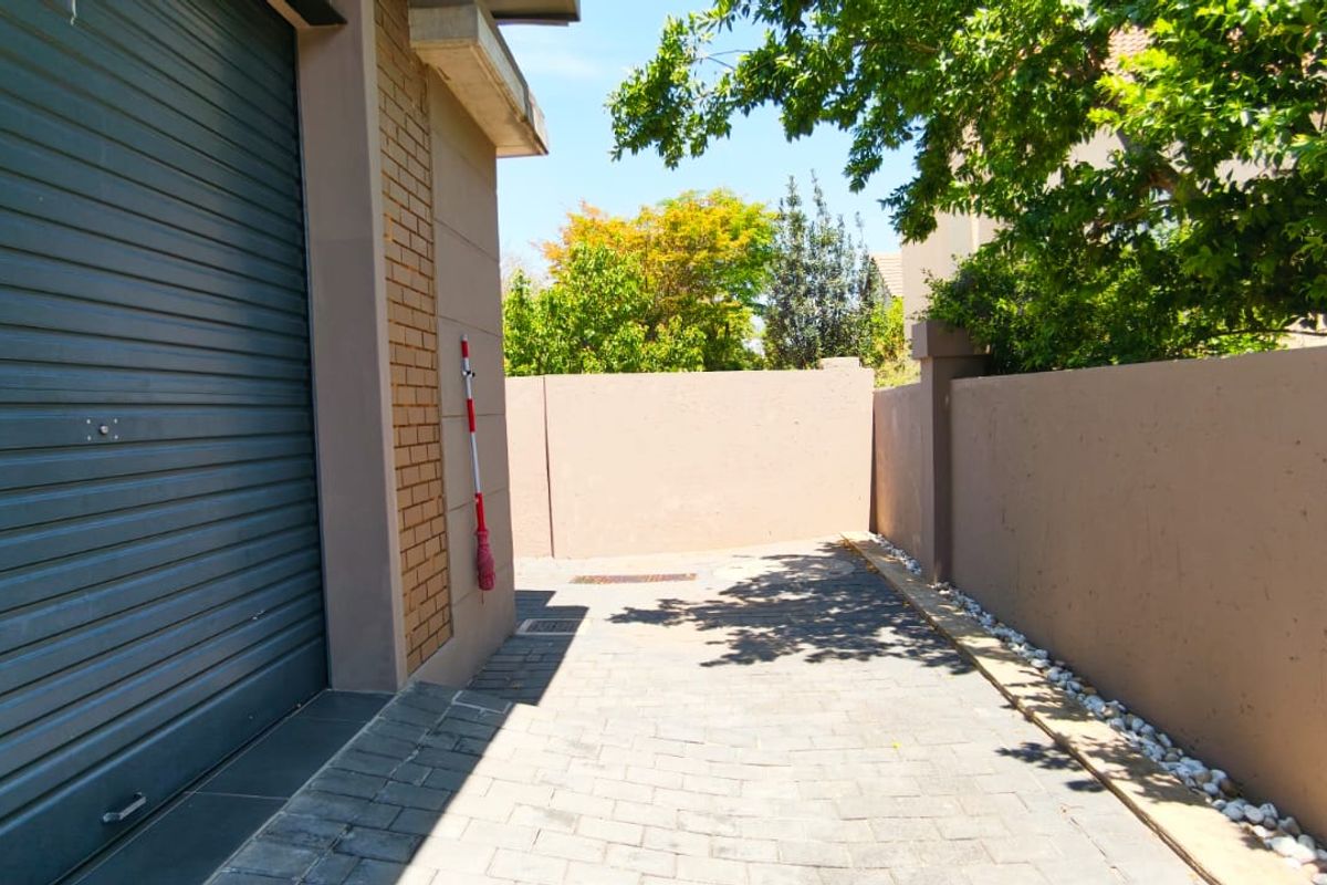 A private paved side yard area featuring a secure roller garage door and high boundary walls, providing a clean and functional outdoor space.