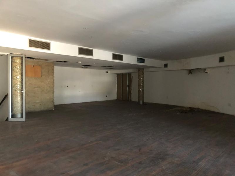 A large, vacant open-plan retail space featuring hardwood flooring, recessed air conditioning vents, and a decorative stone feature wall, currently requiring renovation.
