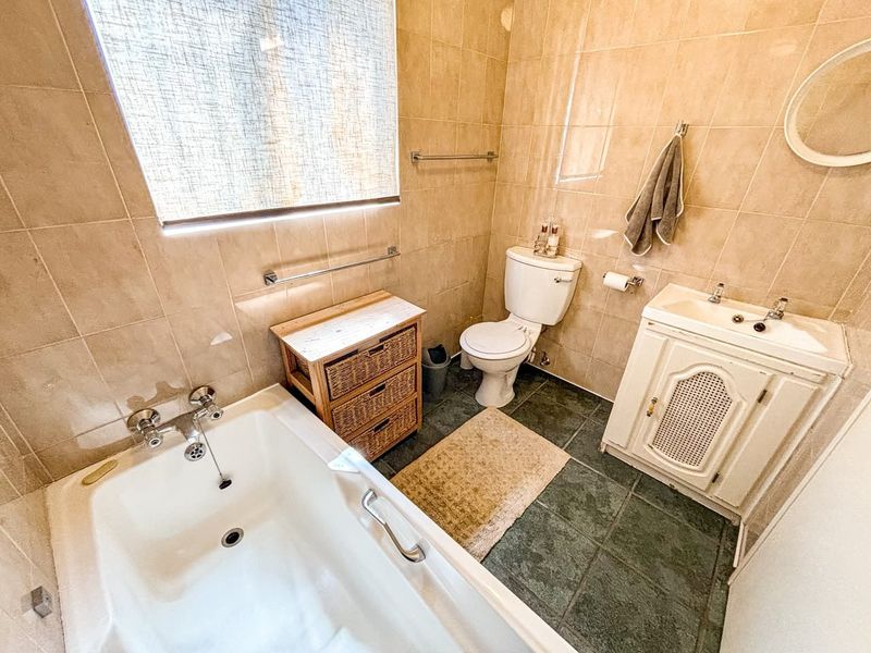 A functional bathroom featuring a bathtub, toilet, and vanity cabinet with tiled walls and flooring throughout.