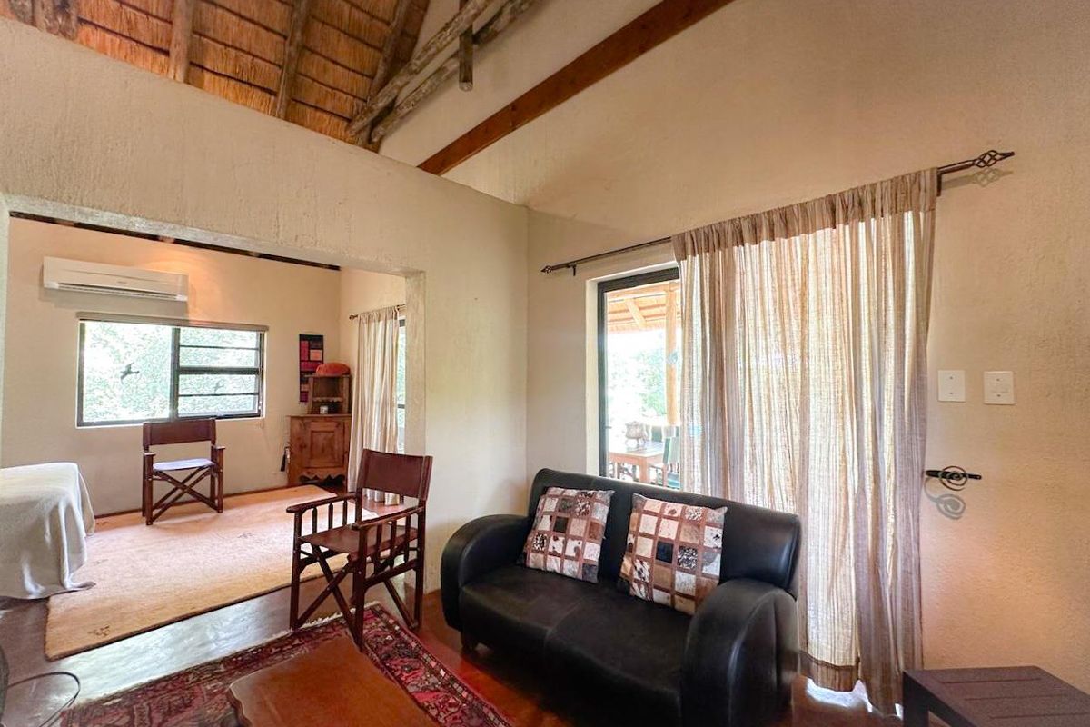 A living area featuring a high vaulted thatched ceiling with exposed timber beams, tiled flooring, and direct access to an outdoor patio.