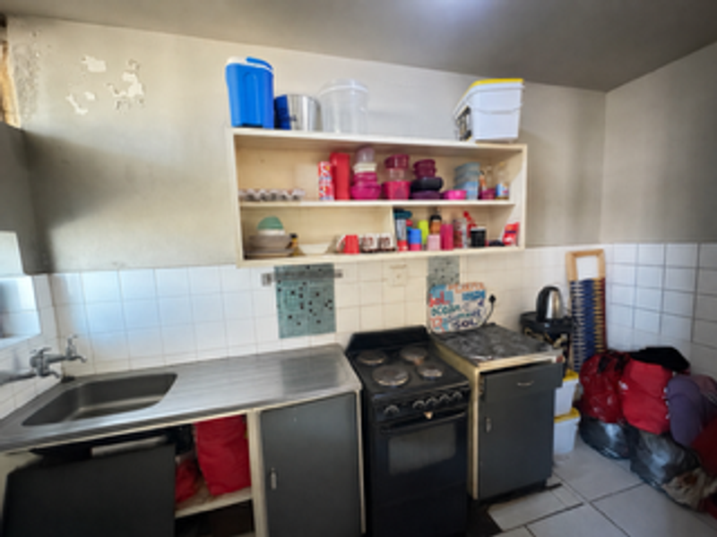 A compact kitchen featuring a stainless steel sink, electric stove, tiled backsplash, and open wall-mounted shelving.