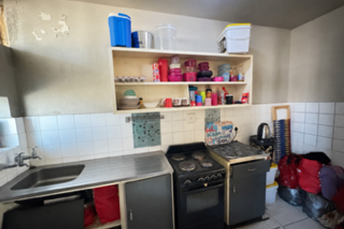 A compact kitchen featuring a stainless steel sink, electric stove, tiled backsplash, and open wall-mounted shelving.