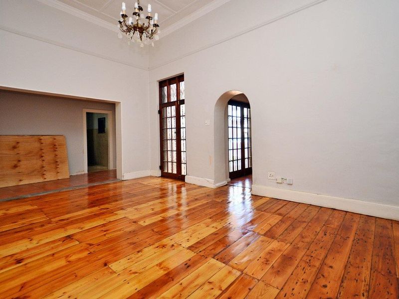 Spacious living area featuring polished hardwood floors, classic crown molding, an elegant chandelier, and charming arched doorways leading to adjacent spaces.