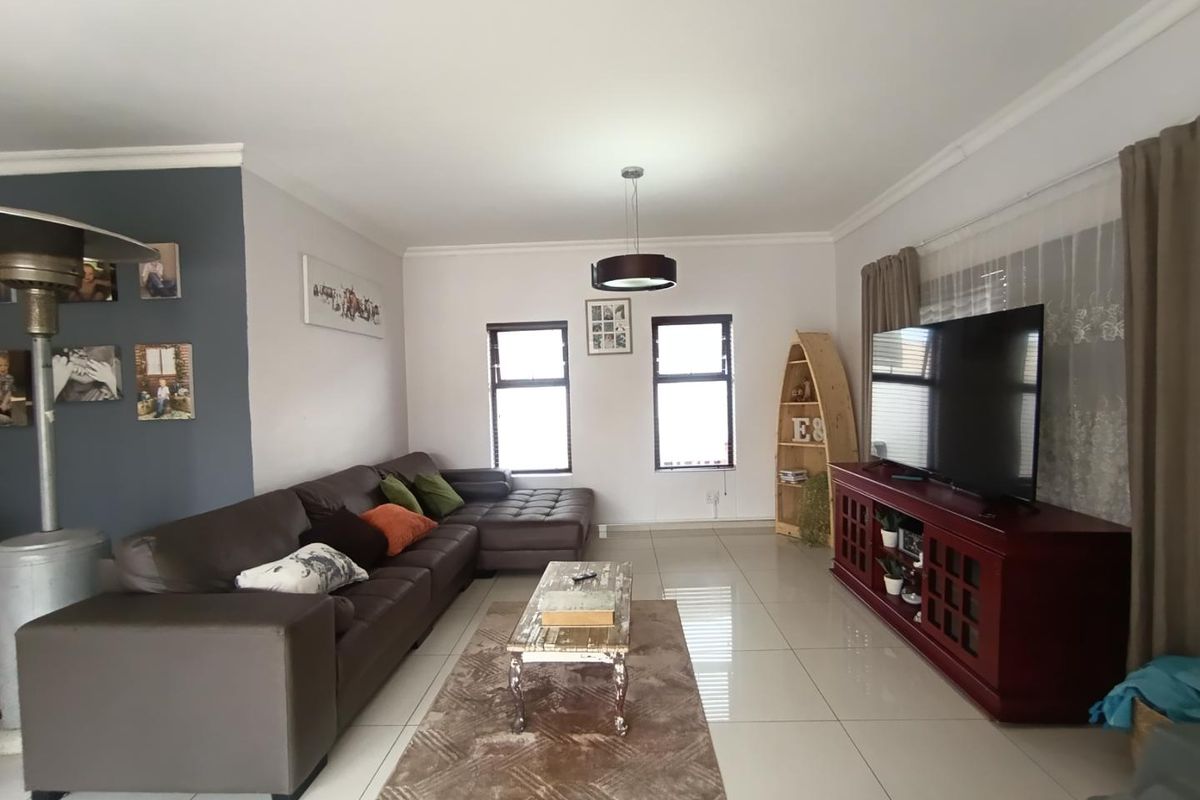 A spacious living room featuring large format floor tiles, neutral wall finishes, and a feature wall, providing a comfortable and well-lit family living space.