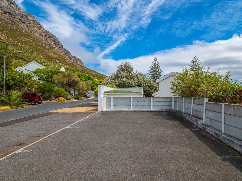 An open-air paved driveway area enclosed by precast concrete boundary walls, situated in a residential street setting with mountain views.