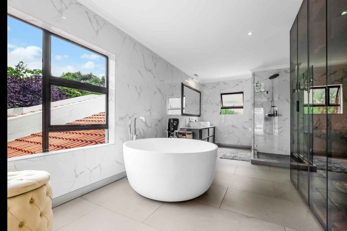 Modern bathroom featuring a freestanding soaking tub, large walk-in glass shower, marble-look wall tiling, and sleek dark cabinetry.