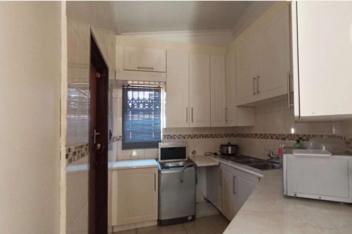 A functional kitchen featuring white cabinetry, tiled backsplash, double basin sink, and dedicated space for laundry appliances.