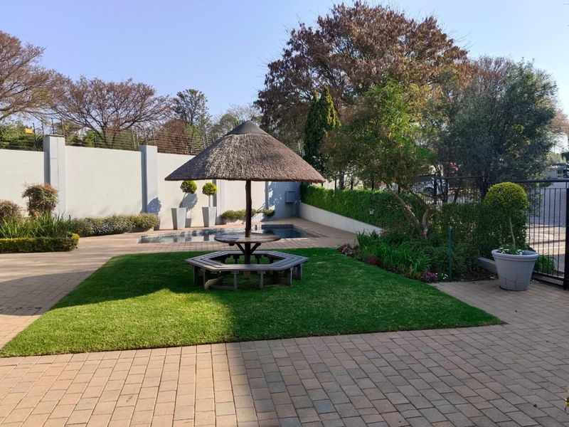 Well-maintained outdoor pool area featuring a paved patio, landscaped lawn, and a traditional thatched lapa, secured by perimeter walls with electric fencing.