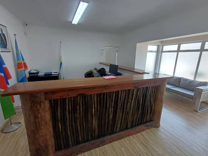 A functional office reception area featuring a custom wooden desk, laminate flooring, and large windows providing natural light.