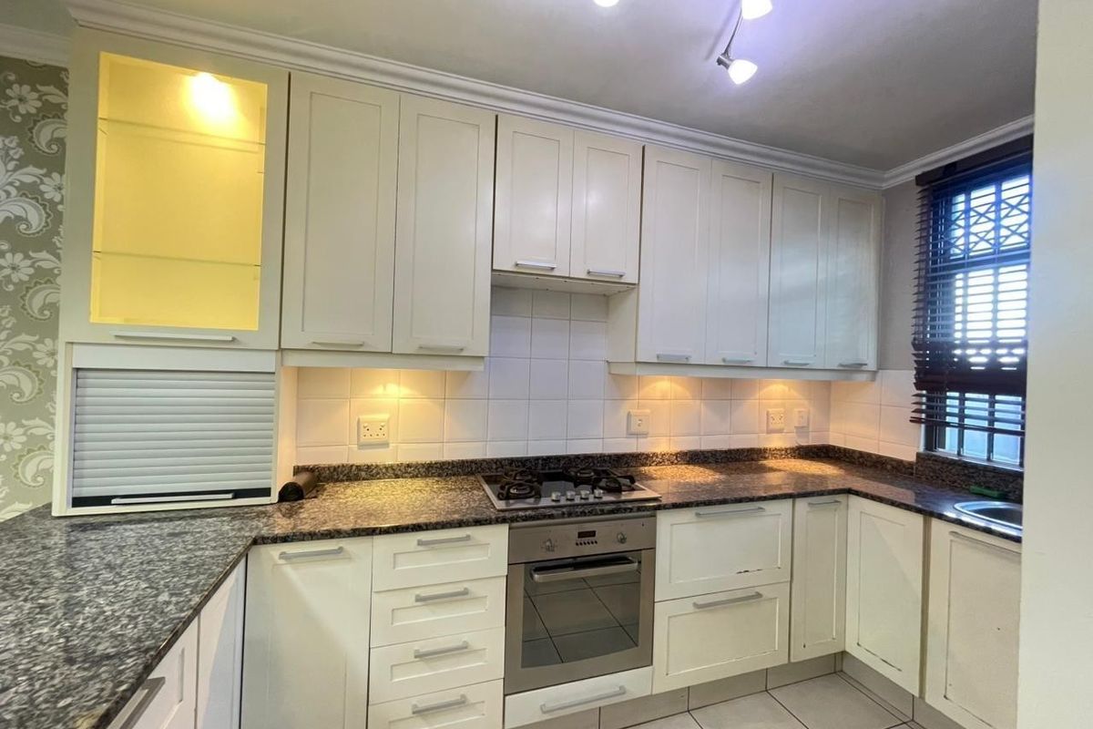 A functional kitchen featuring granite countertops, built-in oven, gas hob, and ample cabinetry with integrated lighting and a tiled backsplash.