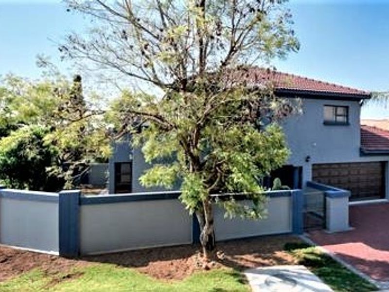 Front exterior view of a two-story house featuring a paved driveway, garage, and perimeter boundary wall.