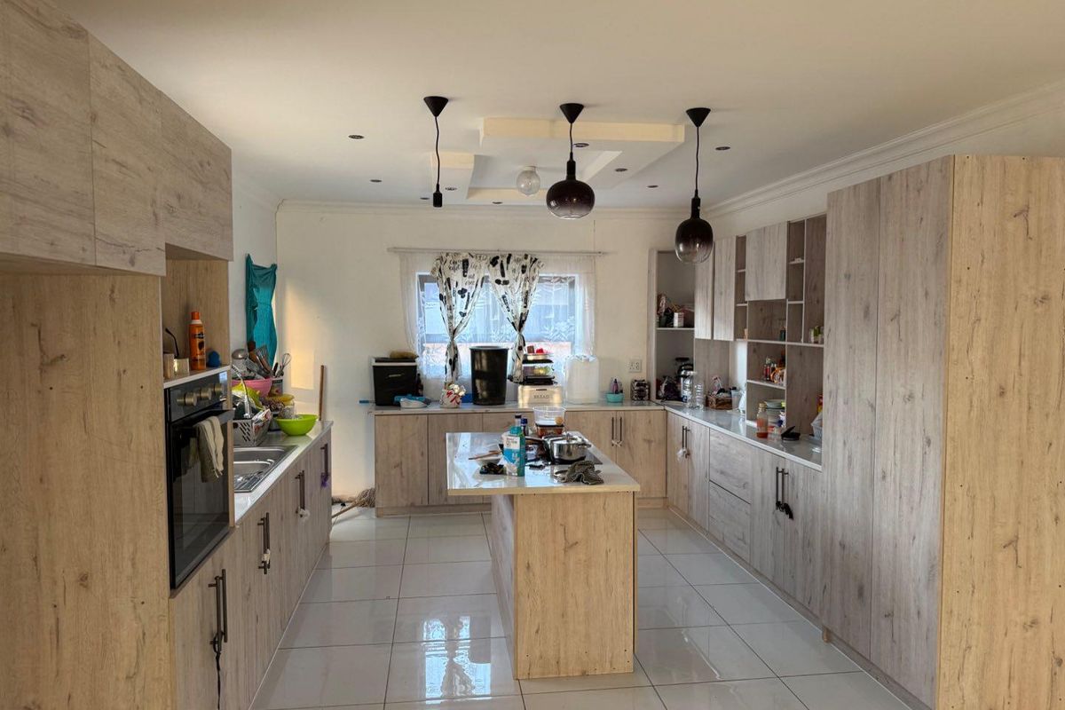 A spacious kitchen featuring light wood-grain cabinetry, a central island, modern pendant lighting, and tiled flooring with ample storage and workspace.