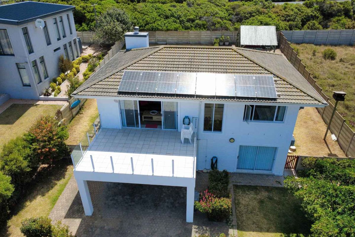 Aerial view of the rear elevation featuring a tiled roof with solar panels, a raised balcony with glass balustrades, and a paved garden area.