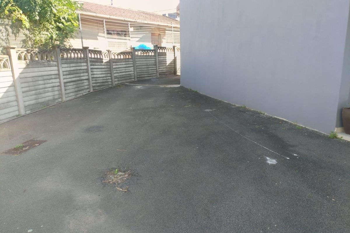 A paved rear exterior area featuring a grey rendered wall and precast concrete boundary fencing, showing signs of wear and surface cracking.