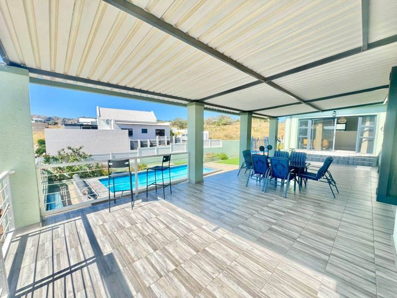 Spacious covered patio featuring tiled flooring and a glass balustrade, overlooking a private swimming pool and landscaped garden area.