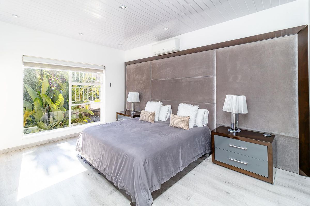 A well-maintained bedroom featuring a large upholstered feature wall, split-system air conditioning, recessed lighting, and light timber-look flooring with garden views.