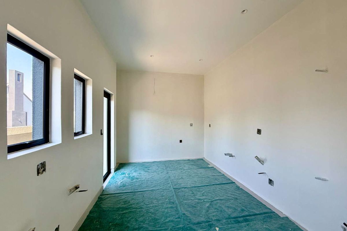 An unfinished kitchen space featuring recessed lighting, black aluminium window frames, and exposed plumbing and electrical points, ready for final cabinetry and appliance installation.