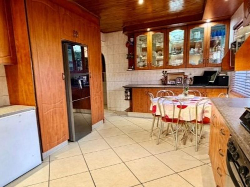A traditional kitchen featuring extensive wooden cabinetry, glass-fronted display units, tiled flooring, and a warm wooden ceiling finish.