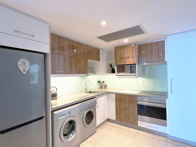 Modern kitchen featuring wood-grain and white cabinetry, stone countertops, integrated appliances, and recessed lighting in a clean, functional layout.