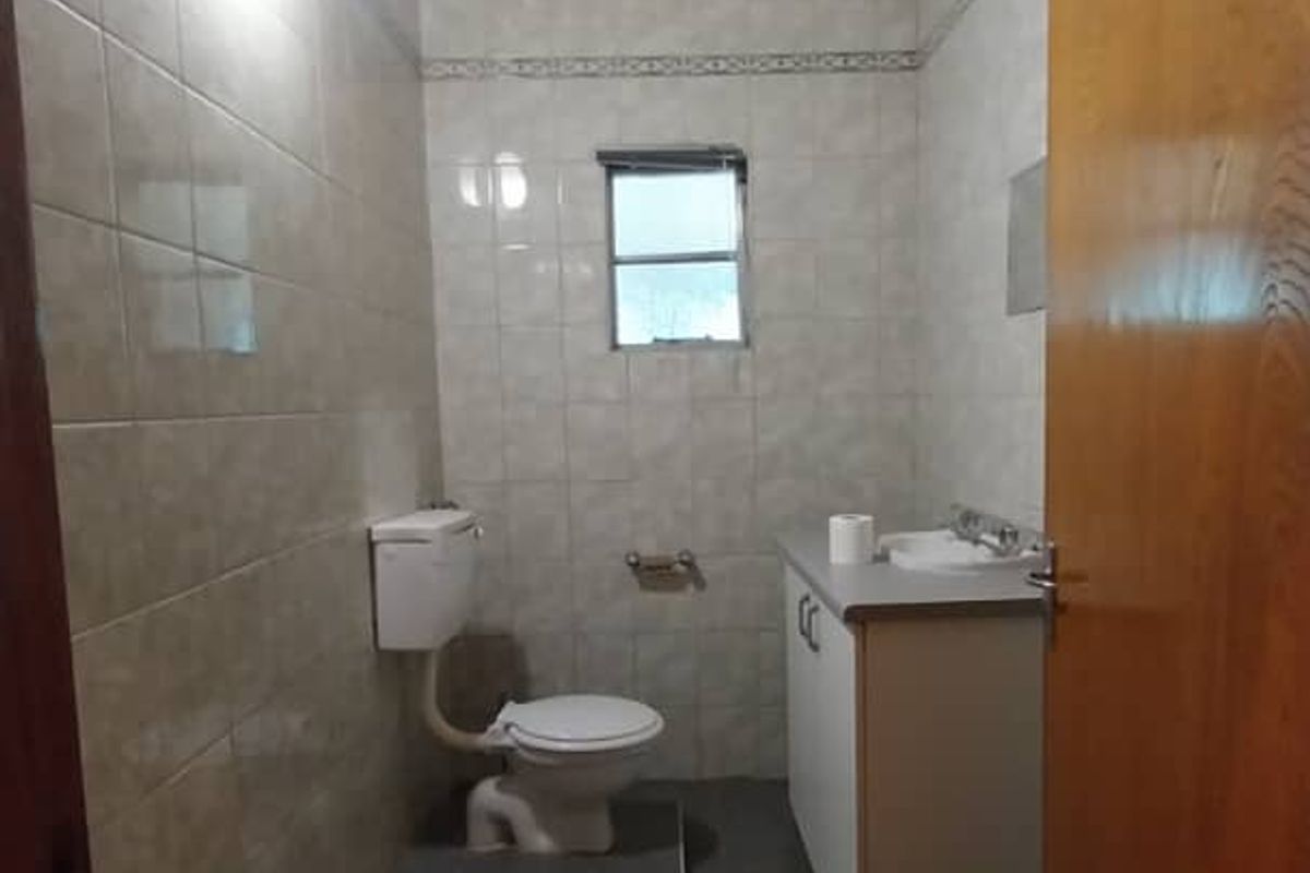 A functional bathroom featuring tiled walls and flooring, a vanity unit with integrated basin, and a toilet.