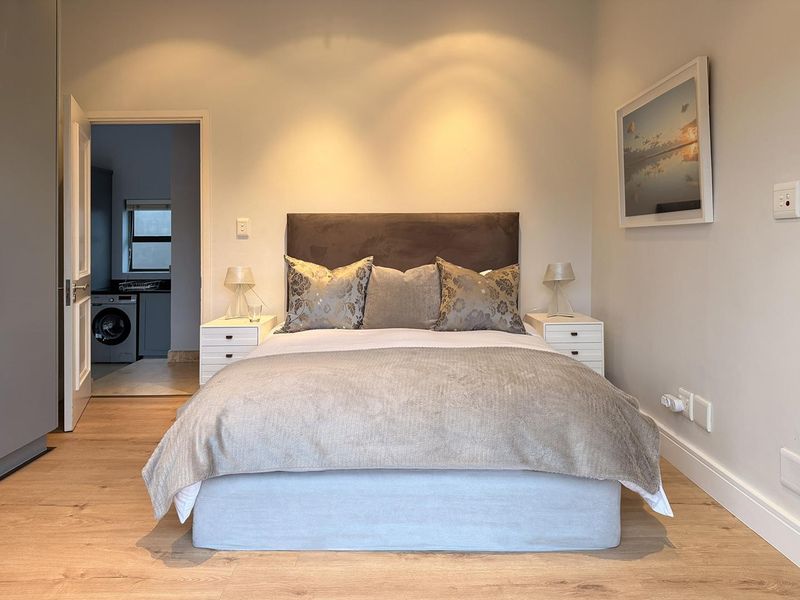 A well-maintained bedroom featuring modern laminate flooring, recessed lighting, and neutral finishes, with an adjacent utility area visible through the doorway.