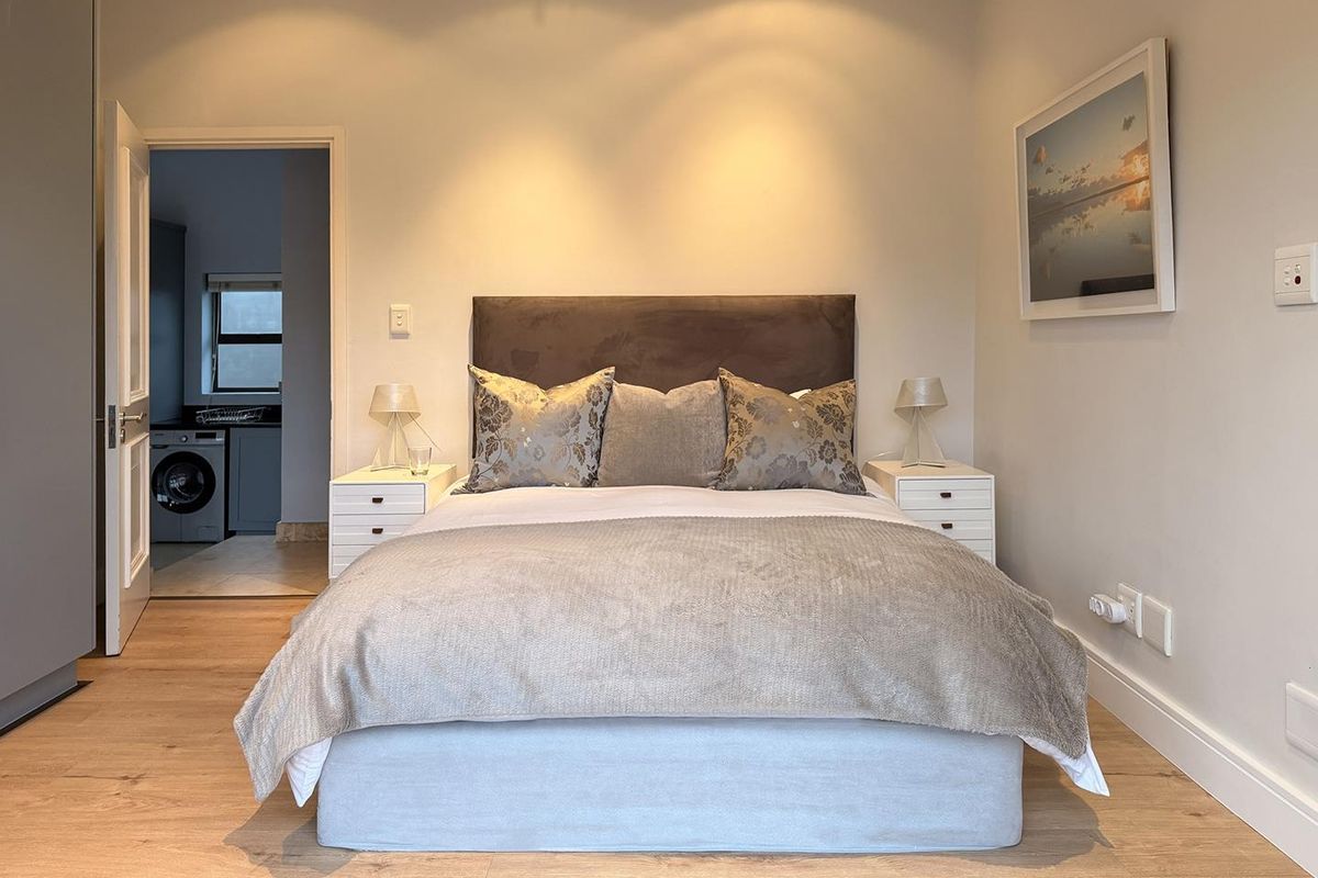 A well-maintained bedroom featuring modern laminate flooring, recessed lighting, and neutral finishes, with an adjacent utility area visible through the doorway.