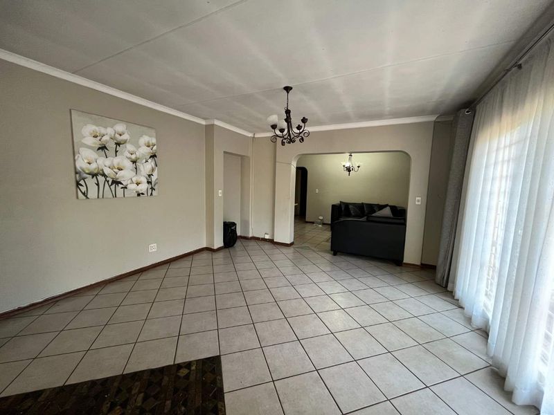 Spacious living area featuring neutral tiled flooring, an arched entryway, and a classic wrought iron chandelier, offering a versatile layout for comfortable family living.