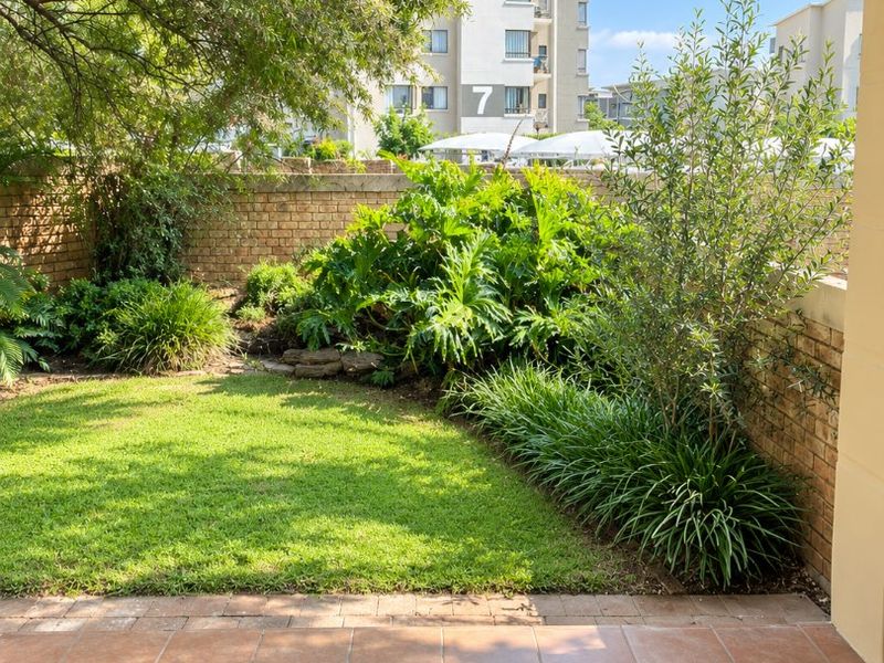 A covered patio area overlooking a private garden with established landscaping and a brick boundary wall.