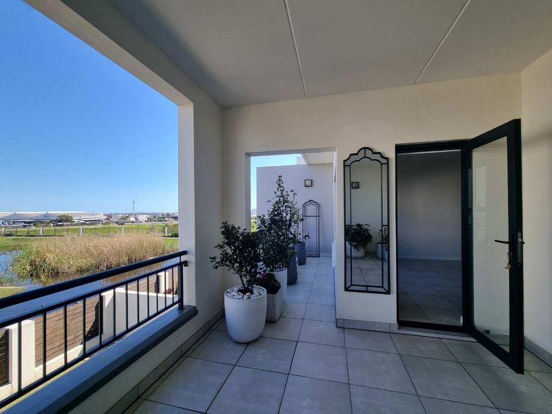 A spacious, well-maintained balcony featuring tiled flooring, a modern metal balustrade, and a scenic view overlooking a tranquil pond and surrounding landscape.