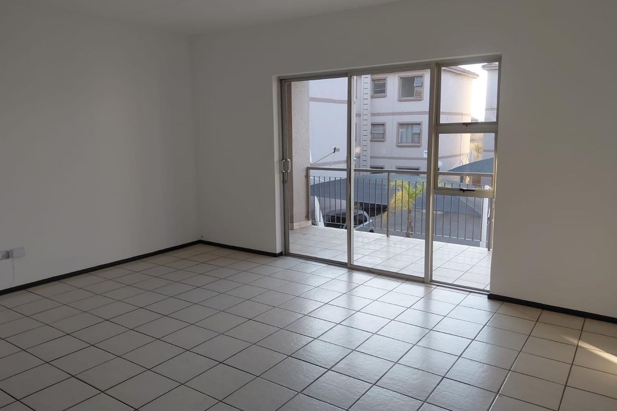 A bright, empty living area featuring neutral tiled flooring and a large sliding glass door providing direct access to a private balcony.
