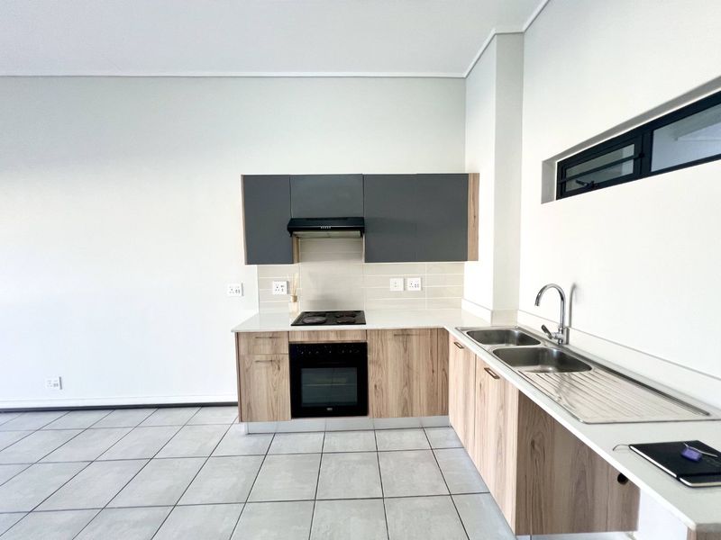 Modern kitchen featuring wood-finish cabinetry, stone countertops, built-in oven, electric hob, extractor fan, and a double sink with tiled flooring.