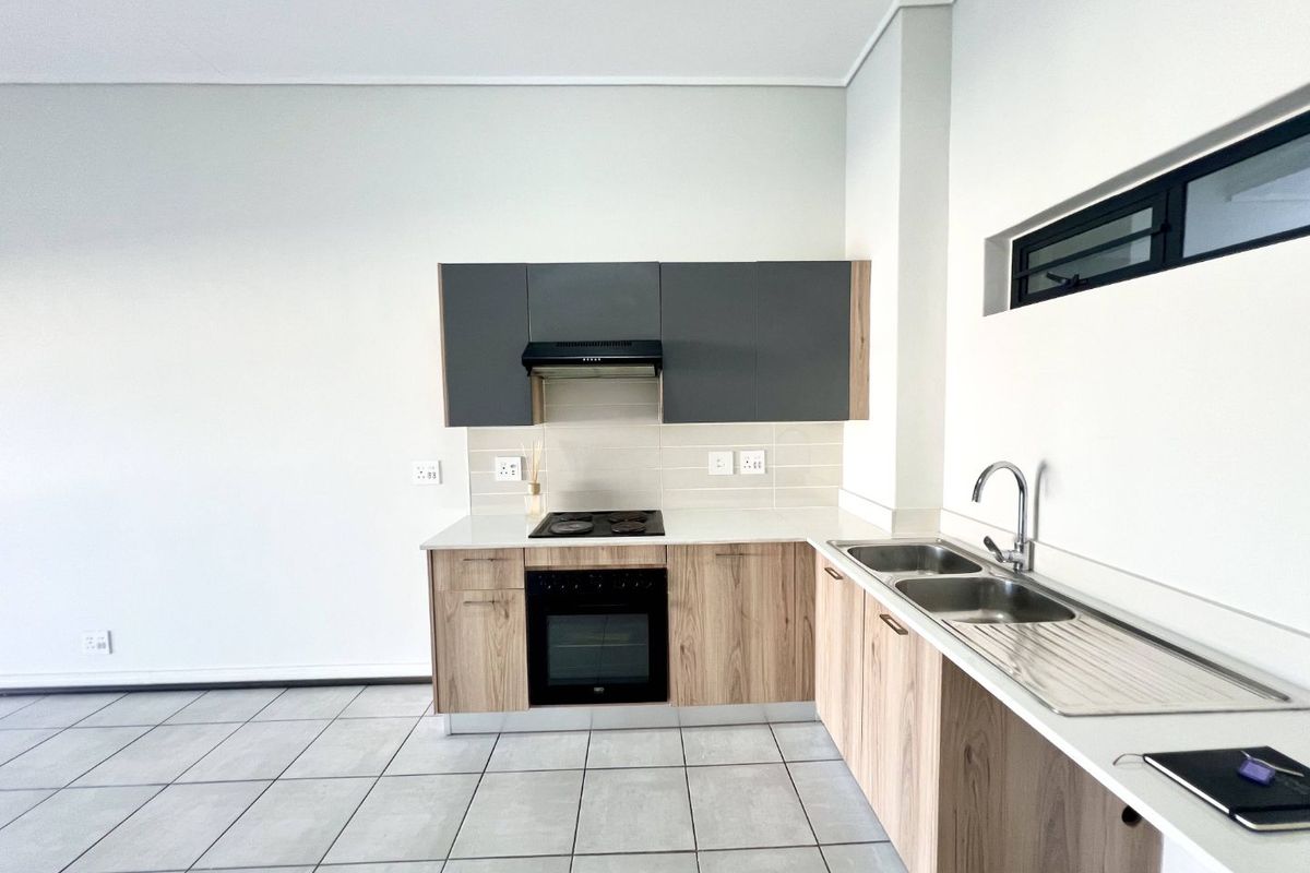 Modern kitchen featuring wood-finish cabinetry, stone countertops, built-in oven, electric hob, extractor fan, and a double sink with tiled flooring.