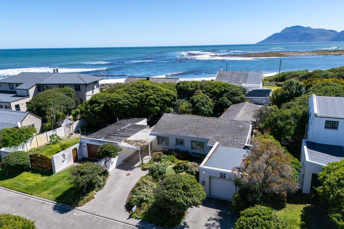 Aerial view of a coastal residential property featuring a paved driveway, garage, and established garden, situated in a prime location near the ocean.