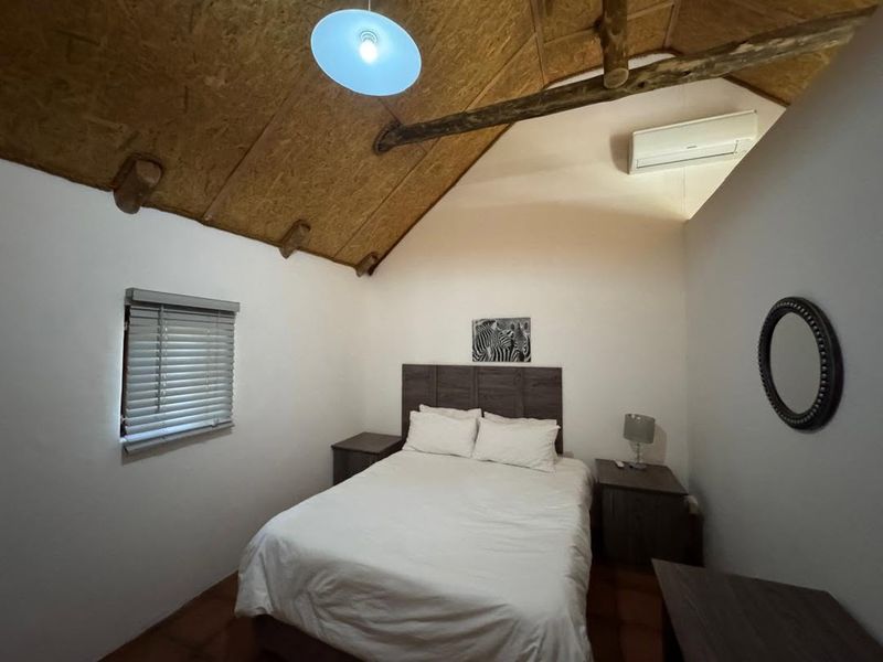 A cozy bedroom featuring a vaulted ceiling with exposed timber rafters, OSB paneling, and a wall-mounted air conditioning unit.