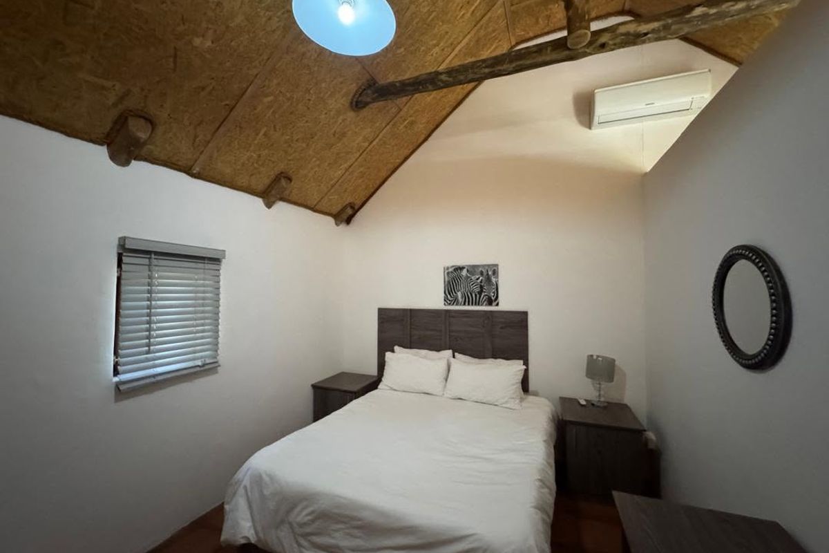 A cozy bedroom featuring a vaulted ceiling with exposed timber rafters, OSB paneling, and a wall-mounted air conditioning unit.