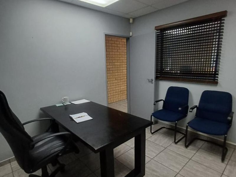 A functional office space featuring tiled flooring, a suspended ceiling with recessed lighting, and a window fitted with venetian blinds.