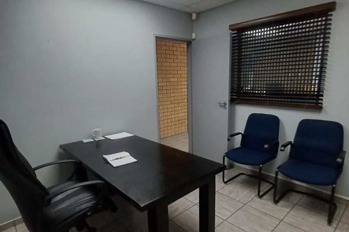 A functional office space featuring tiled flooring, a suspended ceiling with recessed lighting, and a window fitted with venetian blinds.