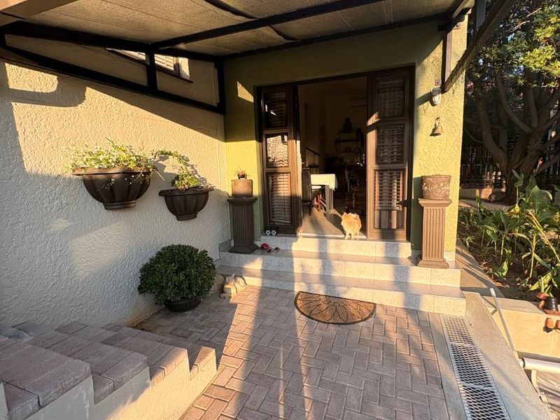 A covered outdoor patio area featuring paved flooring, a drainage channel, and direct access to the interior through double doors.