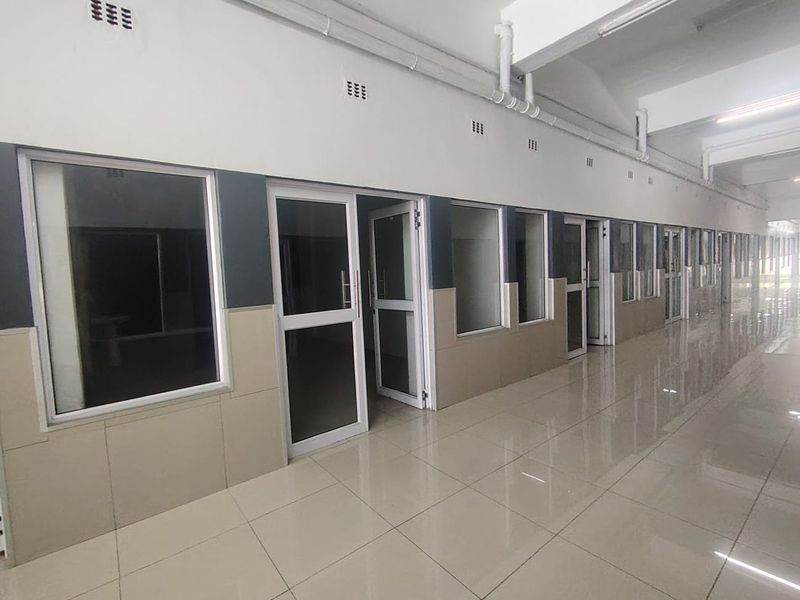 A long, tiled commercial hallway featuring multiple aluminium-framed glass office entrances and exposed ceiling infrastructure.
