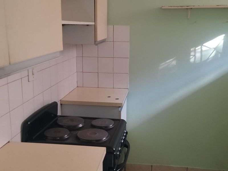 A compact, dated kitchen featuring built-in cabinetry, a tiled splashback, and an electric stove, offering potential for a modern renovation.